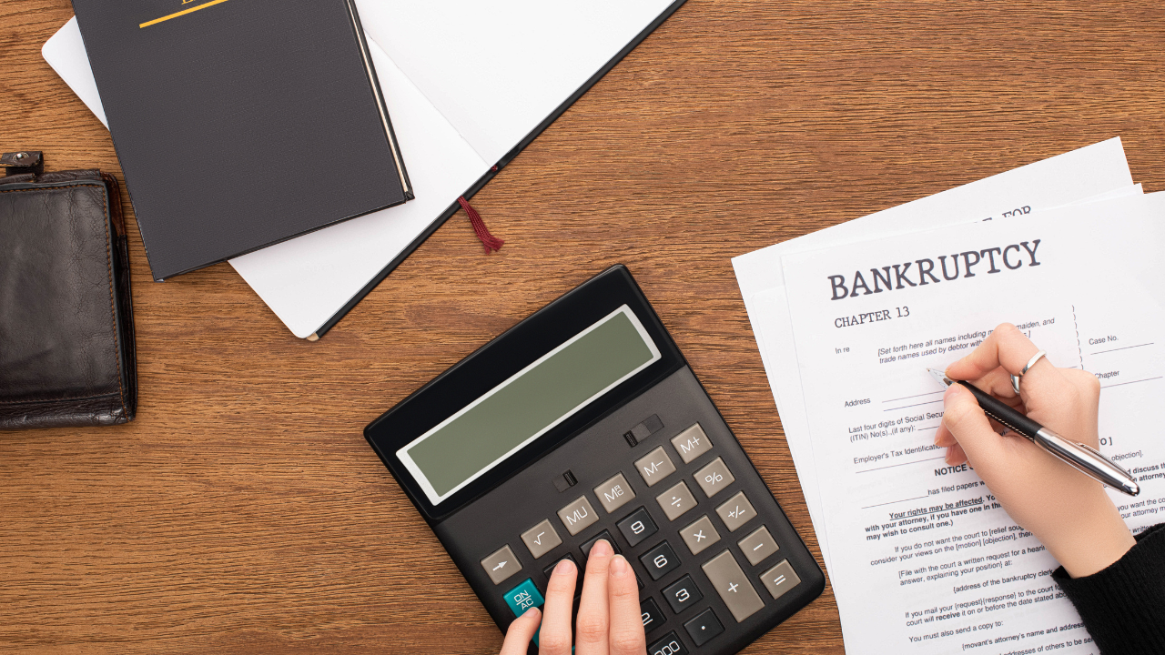 Partial view of woman filling in bankruptcy form and using calculator on wooden background. Image Credit: Adobe Stock Images/LIGHTFIELD STUDIOS