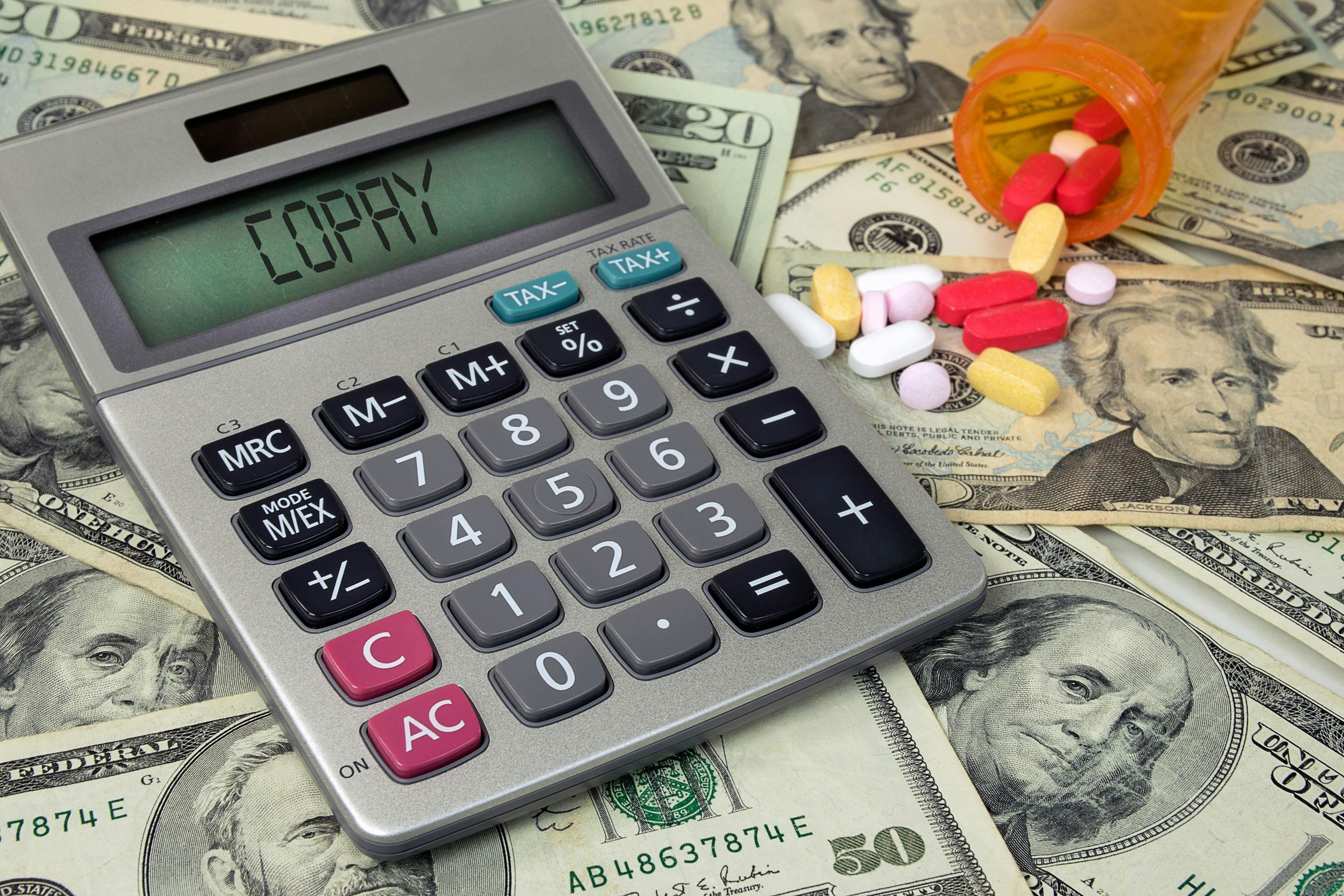 Image credit: driftwood | stock.adobe.com. copay text on calculator with money and prescription pills in bottle