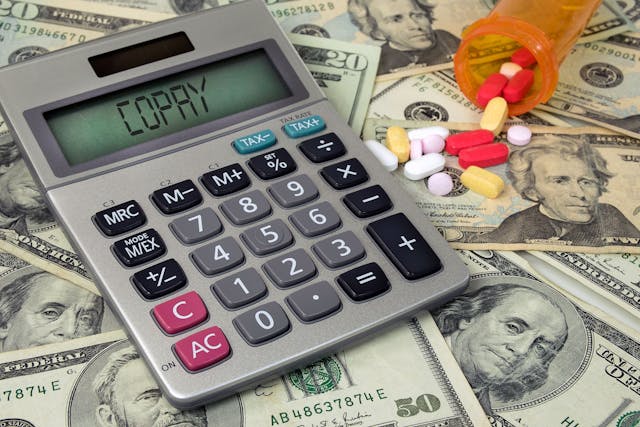 Image credit: driftwood | stock.adobe.com. copay text on calculator with money and prescription pills in bottle