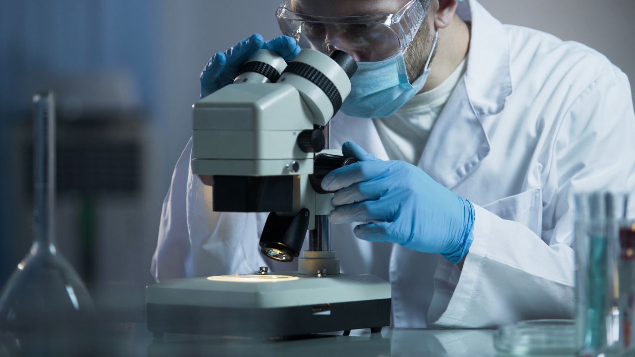 Male scientist looking into microscope, working on AIDS treatment vaccine. Image Credit: Adobe Stock Images/motortion