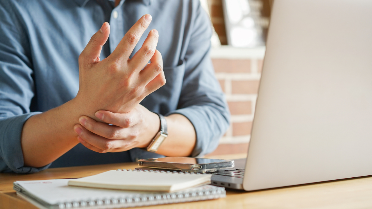 close up employee man massage on his hand and arm for relief pain from hard working on the desktop table at hoe office for stiff or cramp symptom or carpal tunnel syndrome concept. Image Credit: Adobe Stock Images/chinnarach