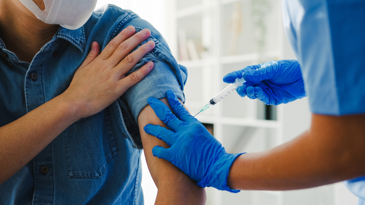 Young Asia lady nurse giving Covid-19 or flu antivirus vaccine shot to senior male patient wear face mask protection from virus disease at health clinic or hospital office. Vaccination concept. Image Credit: Adobe Stock Images/tirachard