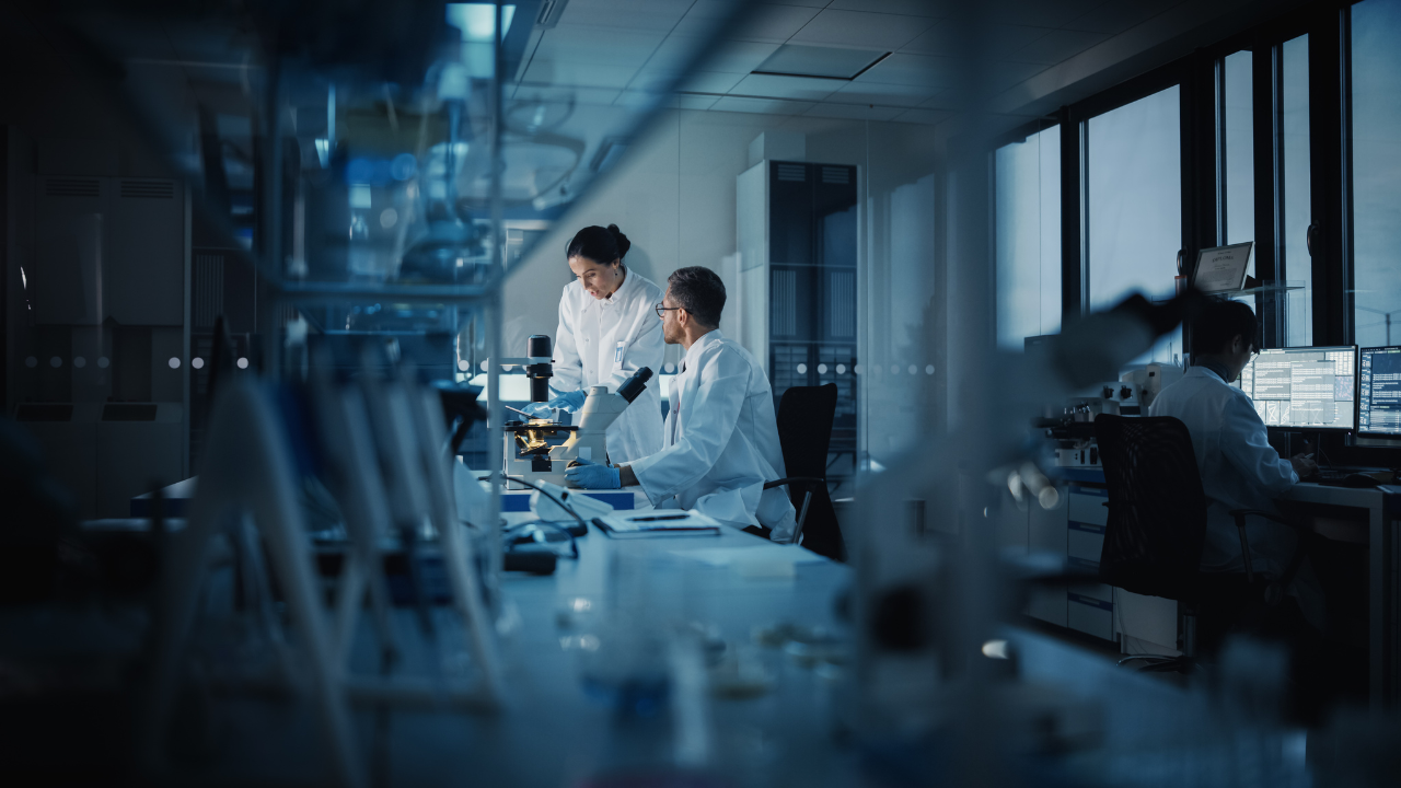 Modern Medical Research Laboratory: Two Scientists Working, Using Digital Tablet, Analyzing Test, Talking. Advanced Scientific Pharmaceutical Lab for Medicine, Biotechnology Development. Evening Time. Image Credit: Adobe Stock Images/Gorodenkoff