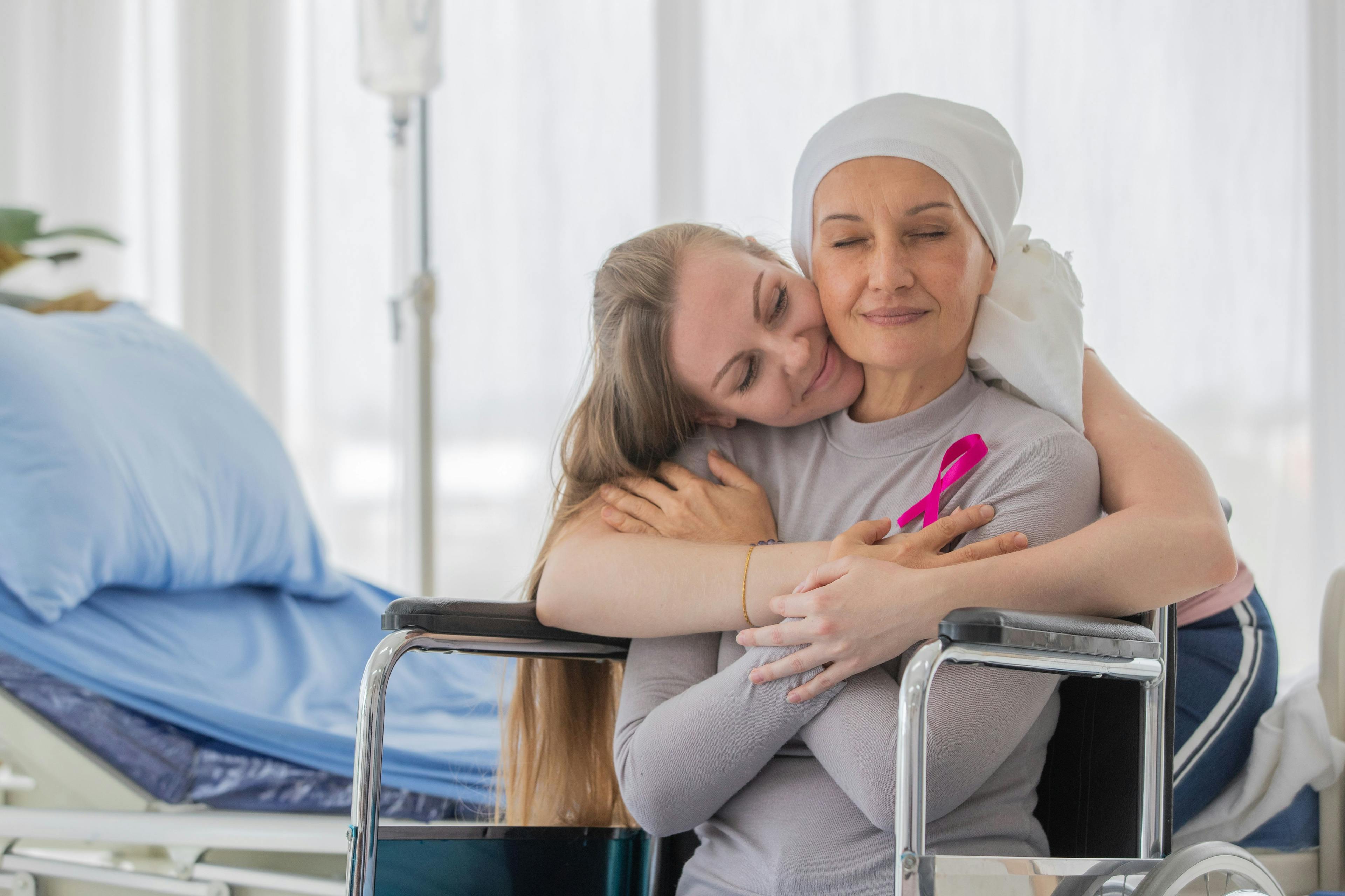A middle-aged breast cancer woman with clothing around her head effected from chemo therapy sitting on wheel chair and hold hand of her daughter with hope and trust in love