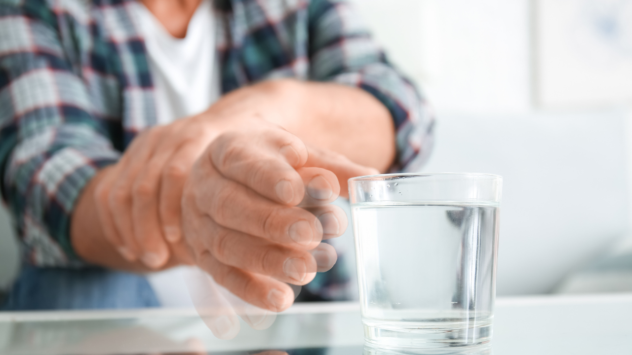 Senior man with Parkinson syndrome taking glass of water from table, closeup. Image Credit: Adobe Stock Images/Pixel-Shot