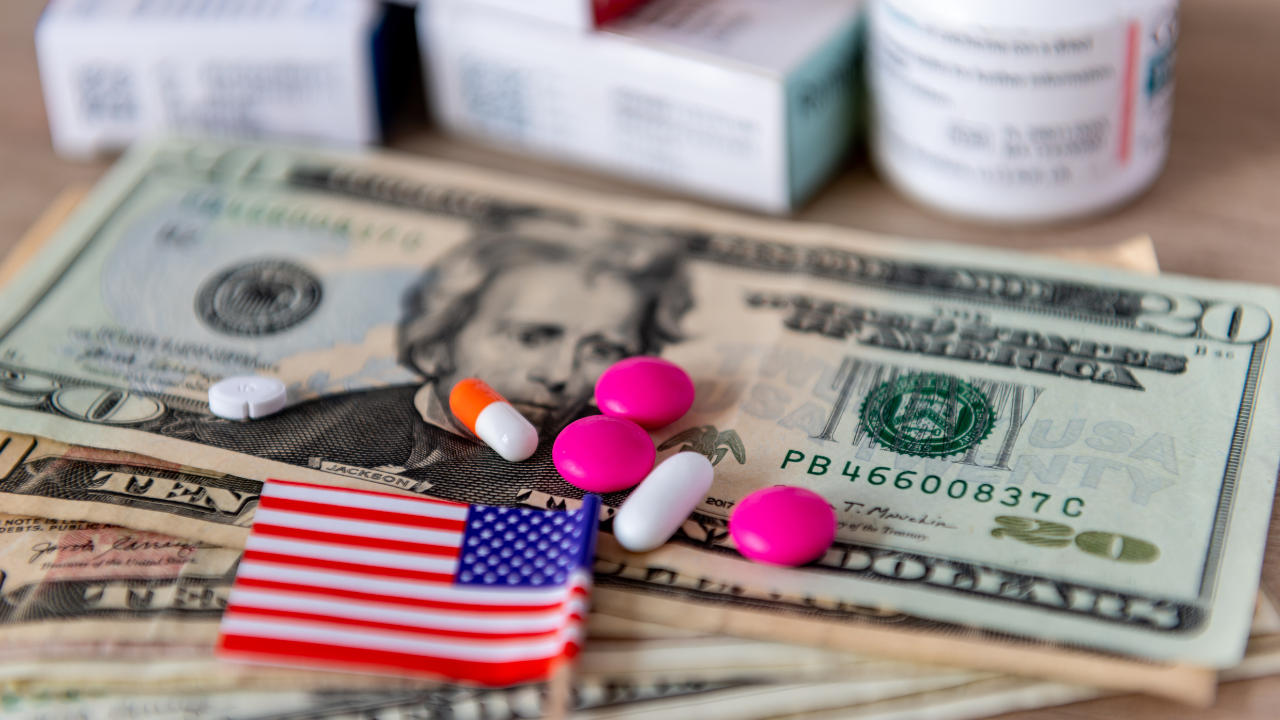 A medical cost, big pharma concept with a glass of water, various medicine, US dollar bills and the American flag. Image Credit: Adobe Stock Images/Ming